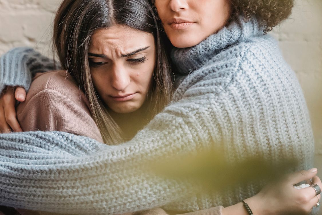 Free Anonymous woman in warn sweater comforting and embracing disappointed female friend near wall in room at home with green leaf Stock Photo