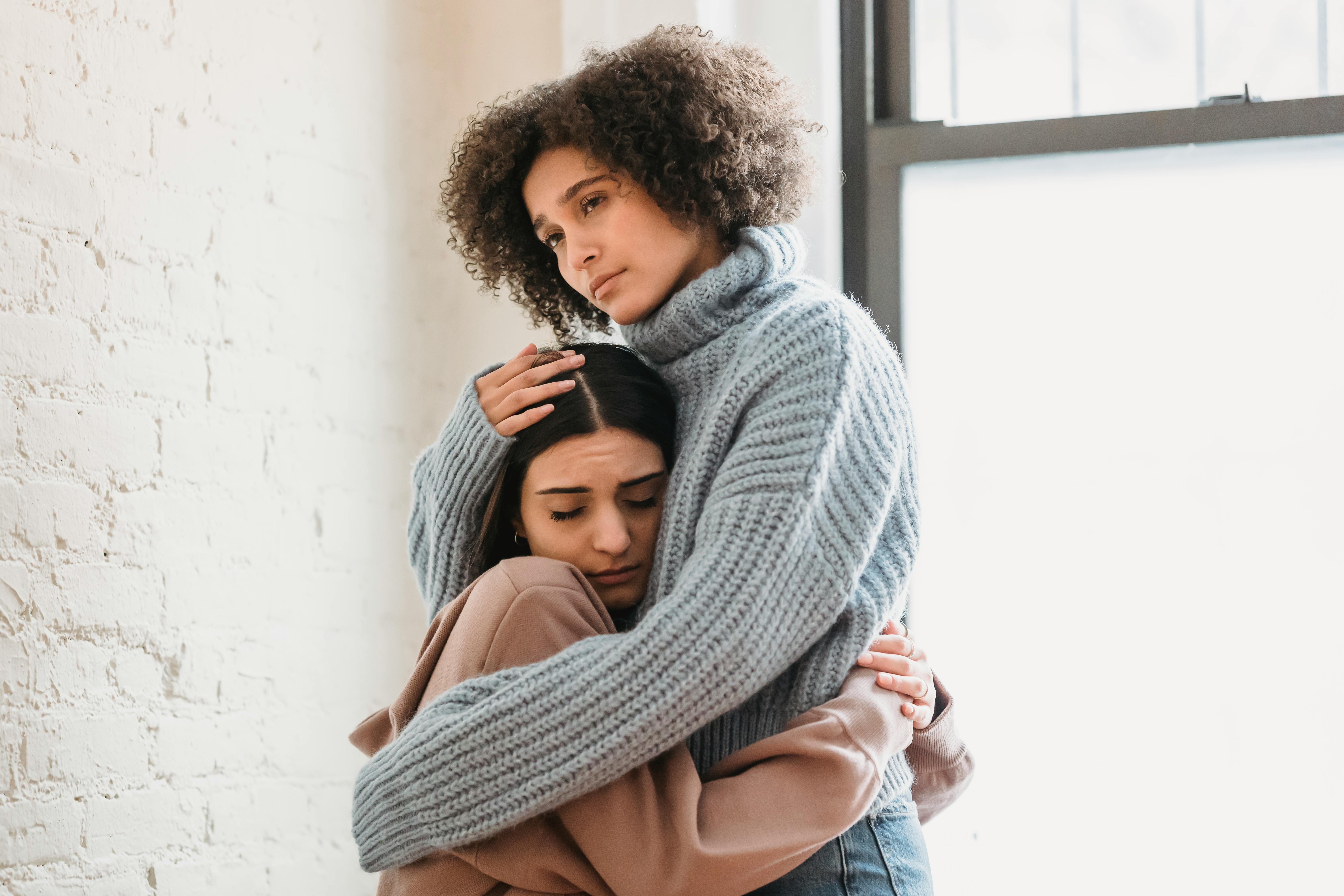 unhappy diverse women hugging in room