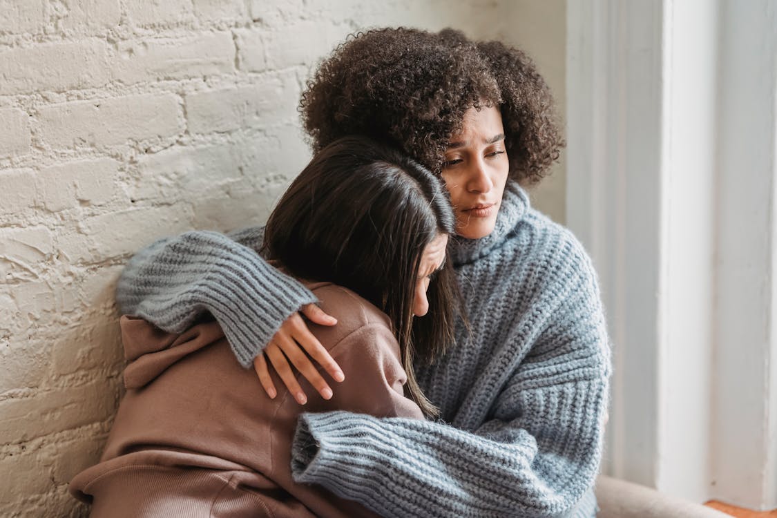 Sad multiracial women hugging at home