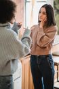 Unrecognizable female pointing at calm female in casual wear while having conflict in light room at home on blurred background