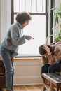 Side view of mad African American female yelling and pointing at sad female sitting in light room during conflict at home