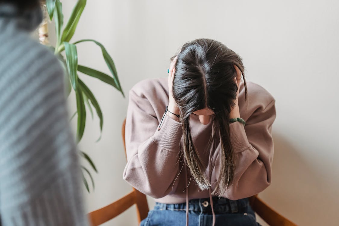 Free Unrecognizable female sitting on chair and covering ears while having conflict with faceless person in light room with green plant at home Stock Photo