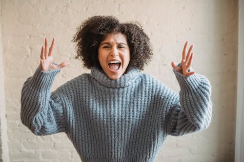 Free Irritated African American female with raised arms looking at camera while shouting loudly near wall in light room at home Stock Photo