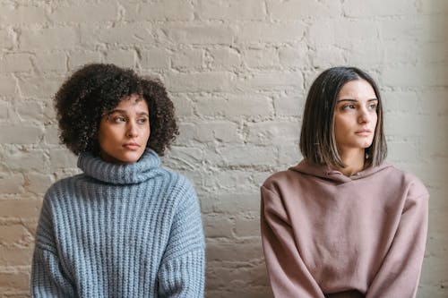 Free Sad African American woman with female friend in casual clothes looking away while sitting in light room during quarrel at home Stock Photo