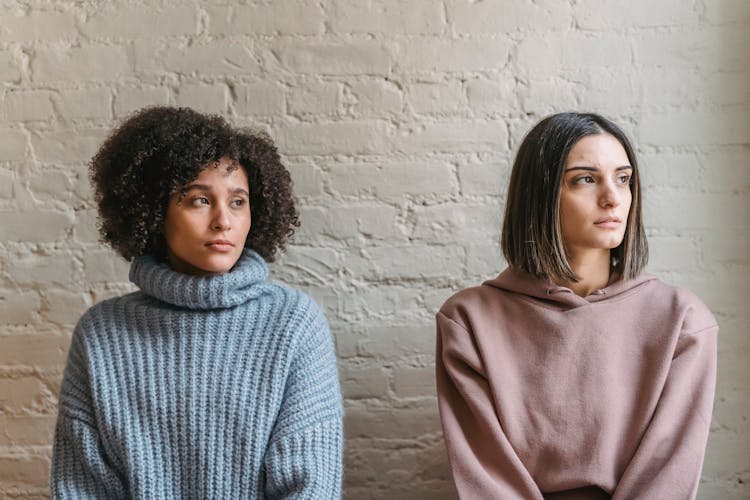 Upset Diverse Women Sitting Near Wall