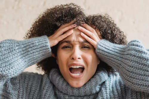 Free Expressive African American woman with curly brown hair touching head and yelling against light background Stock Photo