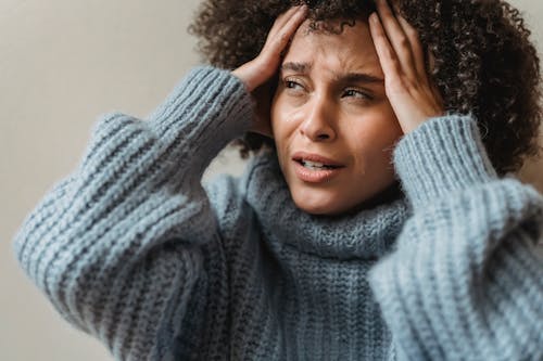 Free Worried African American female with brown curly hair crying and touching head against light wall Stock Photo