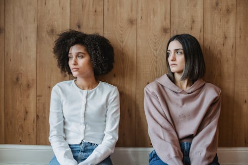 Diverse women sitting near wall and pensively looking away