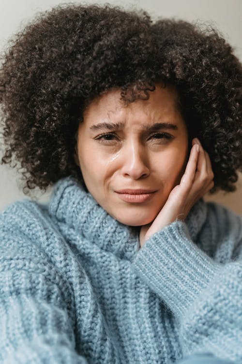 Sad black woman in sweater crying with hand on face