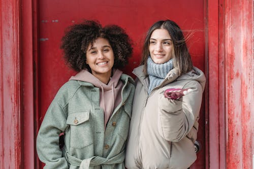 Free Multiracial women in outerwear hugging near red building Stock Photo