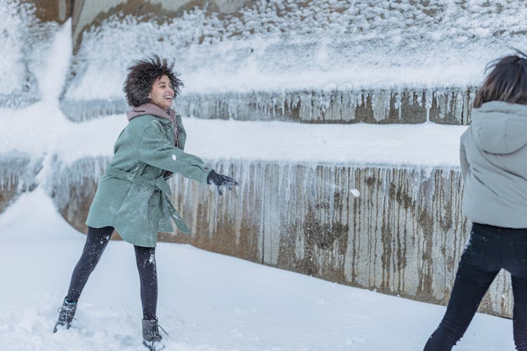 Multiracial Ladies Playing Snowballs In Winter Near Construction In Street