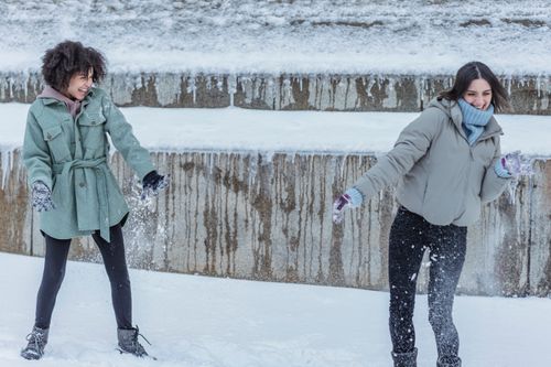 Free Delighted multiethnic girlfriends in outerwear laughing widely while having fun together in winter snowy park Stock Photo