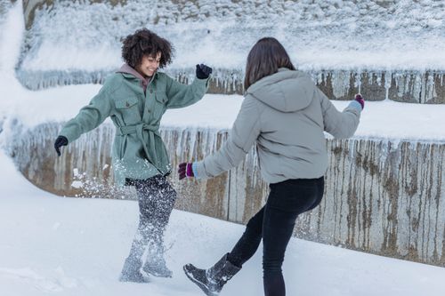 Free Cheerful African American female kicking snow while having fun with playful friend in winter park Stock Photo