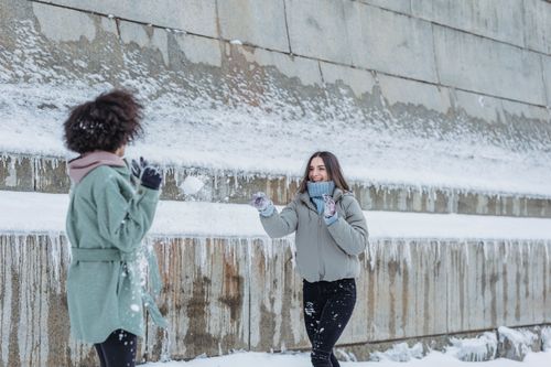 Free Happy female throwing snowball while having fun and playing game with curly haired friend in winter day Stock Photo