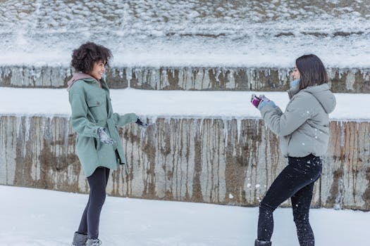 Two women laughing and playing in the snow, enjoying a winter snowball fight outdoors.