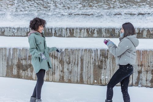 Free Side view of multiethnic female friends wearing outerwear standing opposite each other for snowball fight Stock Photo