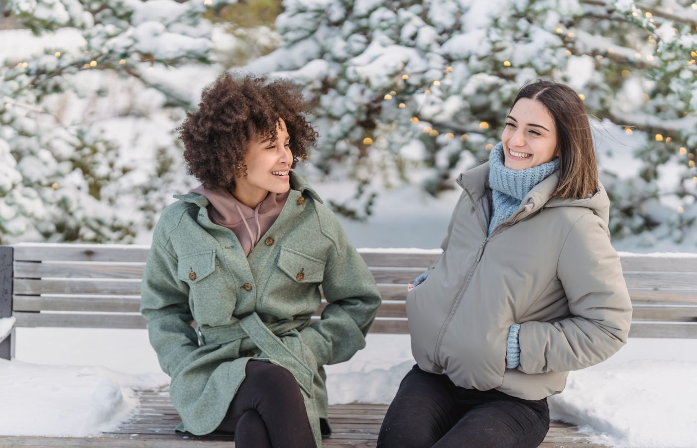 Two friends enjoying a cheerful winter day sitting on a snowy bench outdoors.