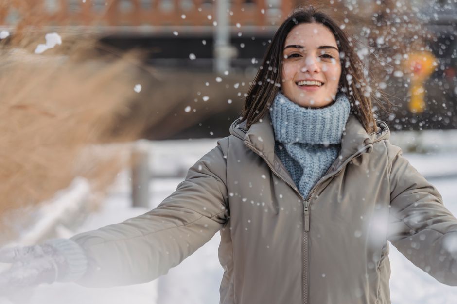 Smiling female in outerwear and warm sweater enjoying winter day and throwing snow in park