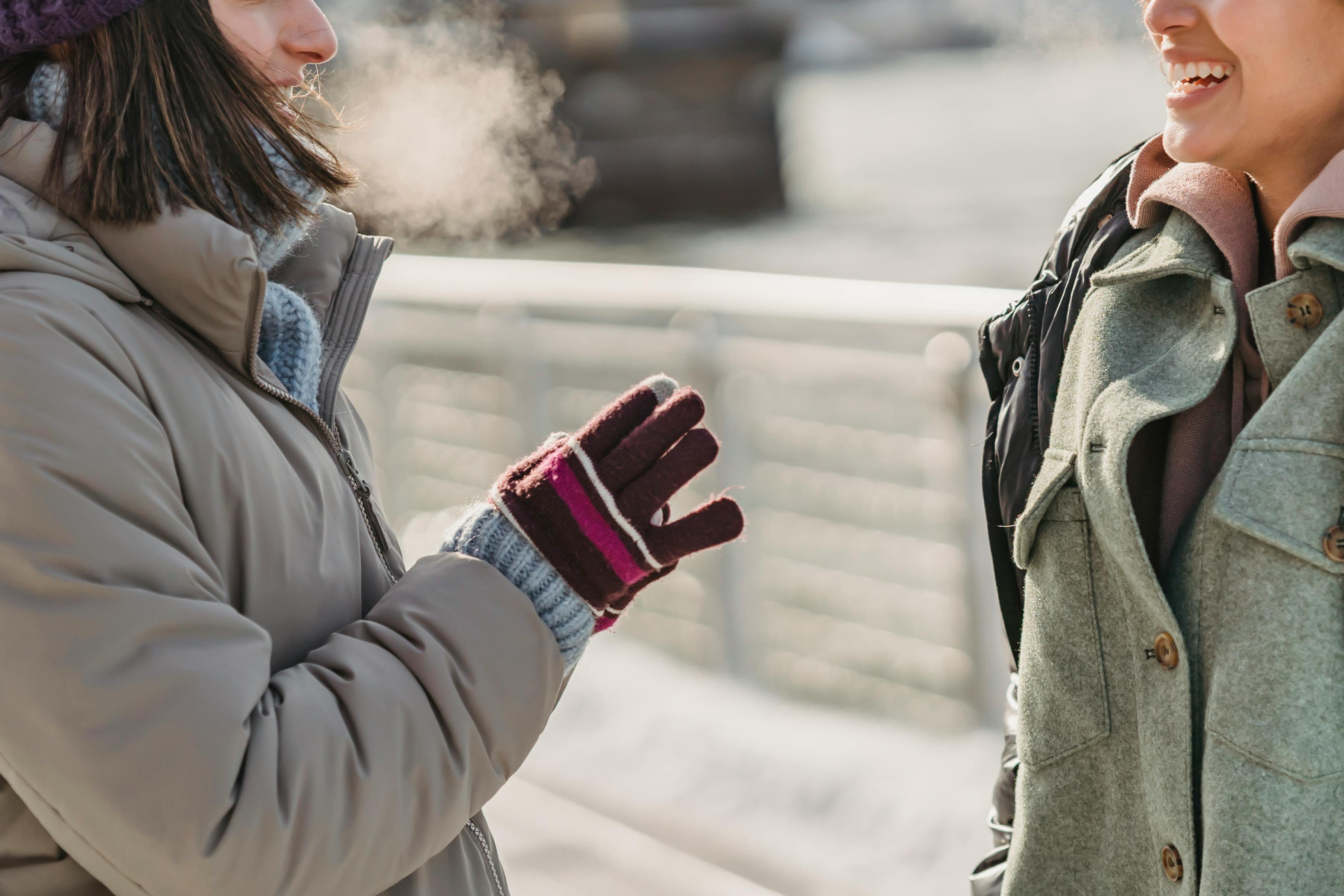 crop happy women talking on city waterfront on cold day