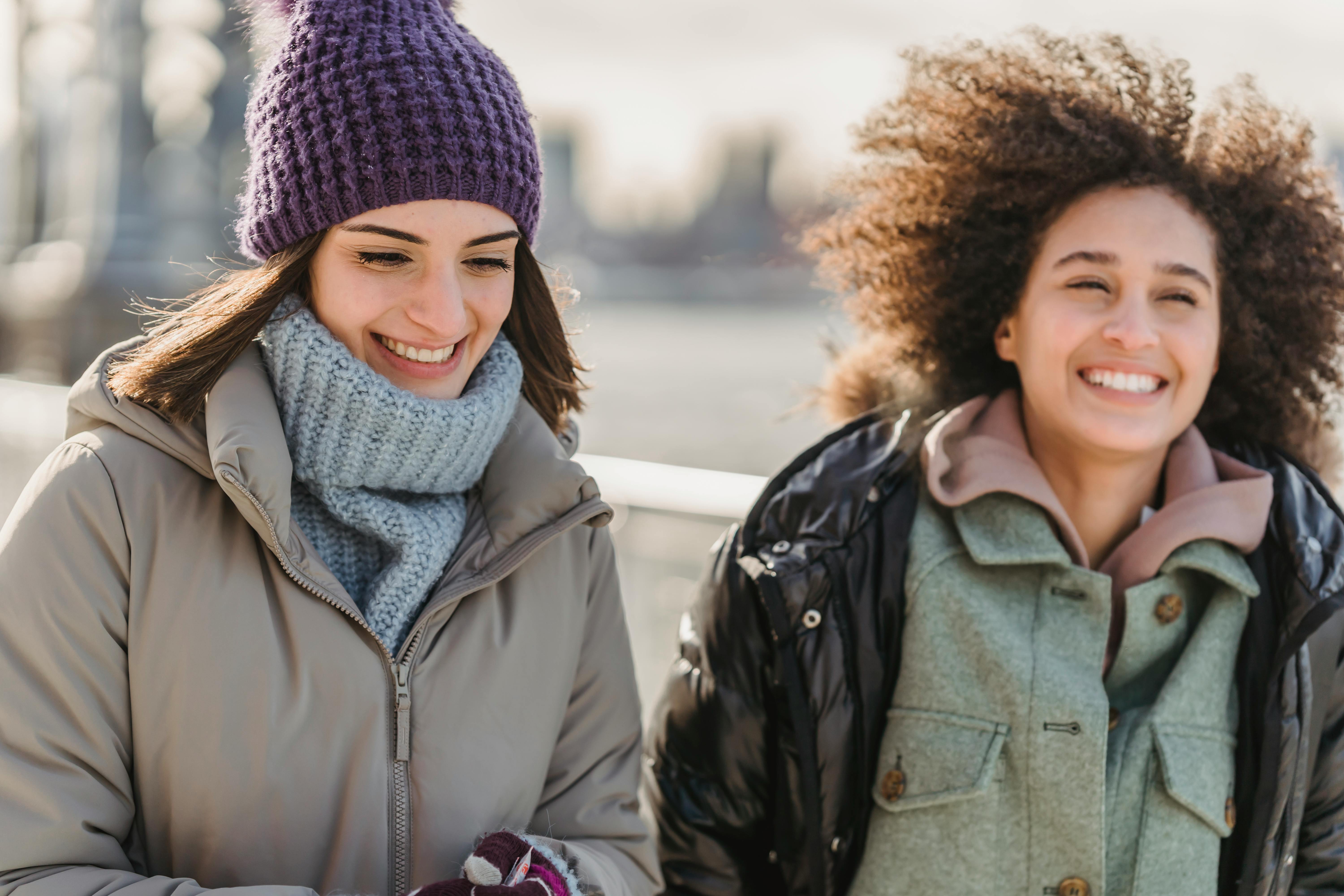 joyful diverse women in outerwear walking together on city riverside