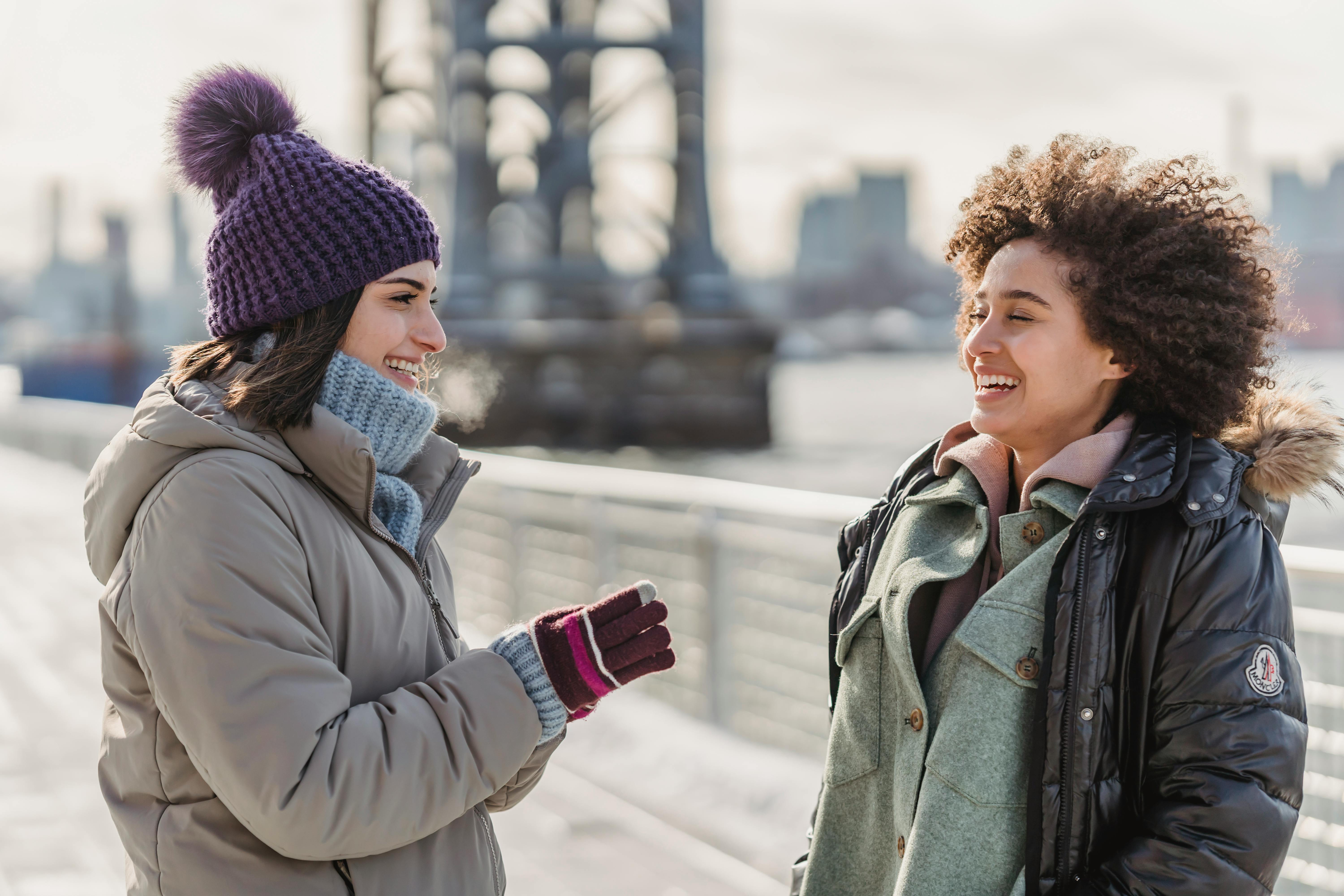 carefree diverse women in outerwear chatting on city embankment