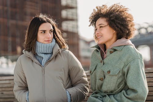 Glad young multiracial female friends in warm clothes chatting and strolling together on city street on cold freezing day