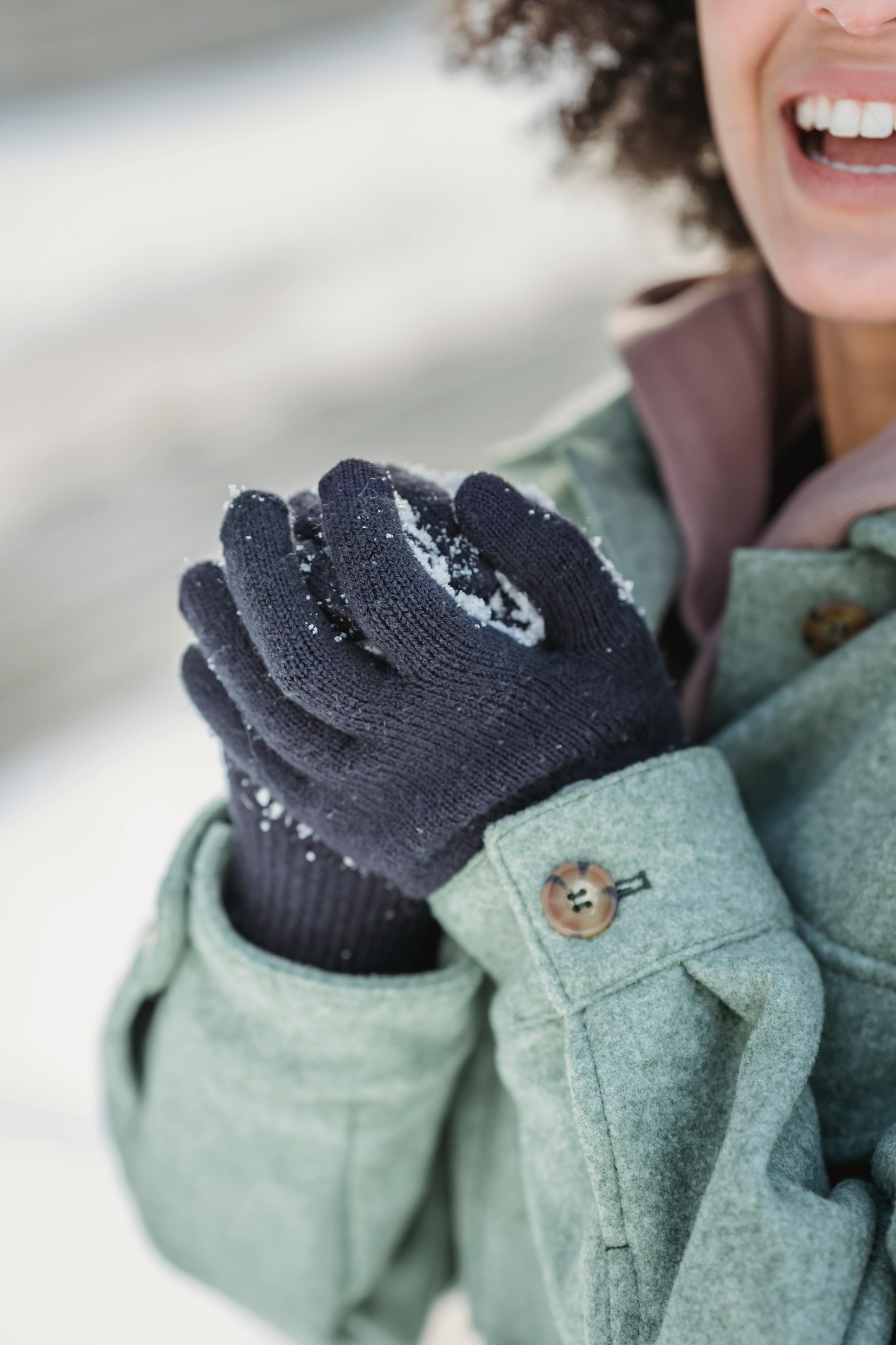 Crop laughing female in warm clothes and mittens holding snowball while playing in snowy cold winter park