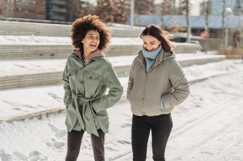 Free Expressive young multiracial female friends wearing warm clothes chatting and walking together with hands in pockets on snowy city street on freezing winter day Stock Photo