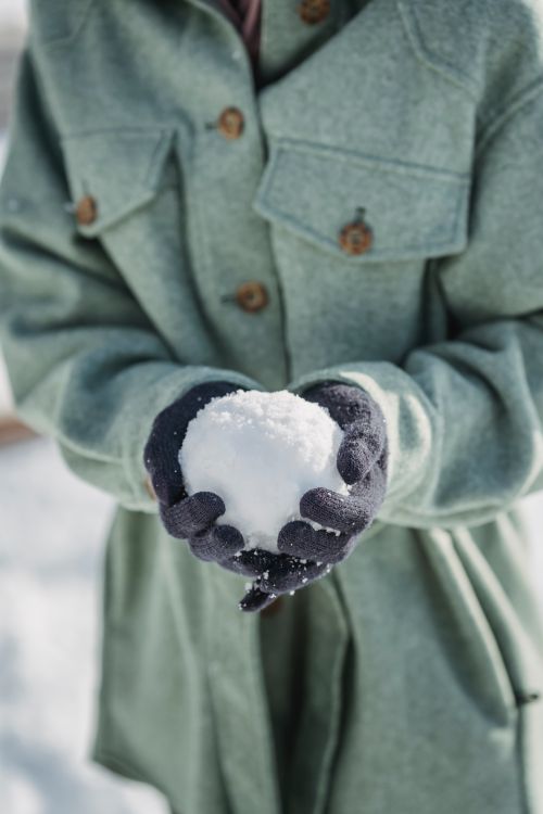 Free Crop unrecognizable female in warm coat and gloves holding snowball while spending sunny winter day in countryside Stock Photo