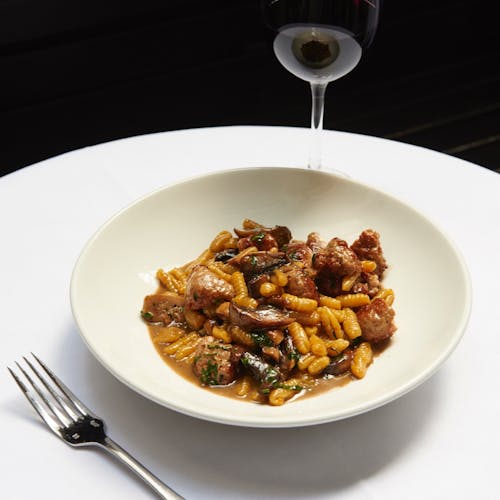 From above of palatable dish with gnocchi pasta and meat in sauce served in white ceramic plate and placed on round table with glass of wine in restaurant