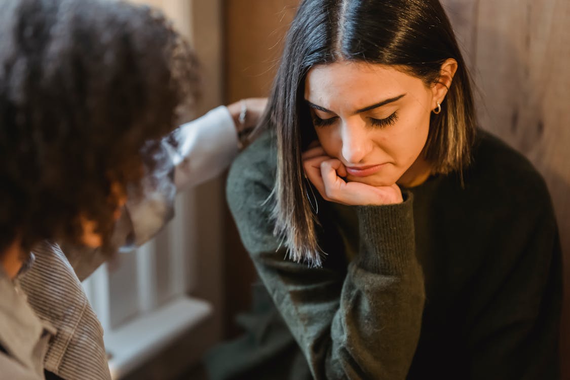 Free Crop woman tapping shoulder and comforting upset female friend while sitting at home together Stock Photo