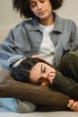 Sad woman lying on knees of ethnic female friend and crying
