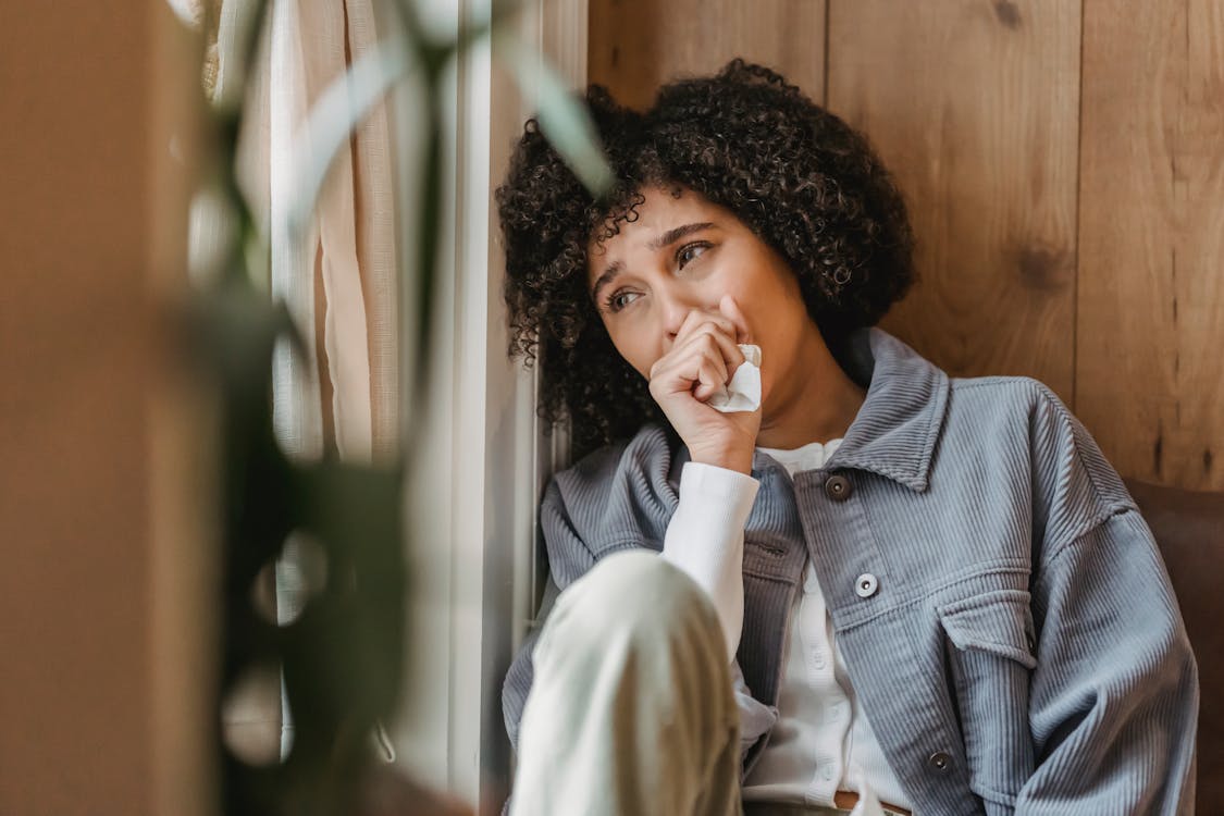 Free Lonely young black lady with Afro hair looking away while sitting near wooden wall and crying Stock Photo
