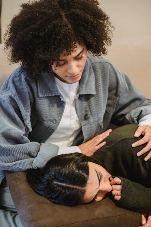 Young ethnic lady calming crying female best friend on sofa