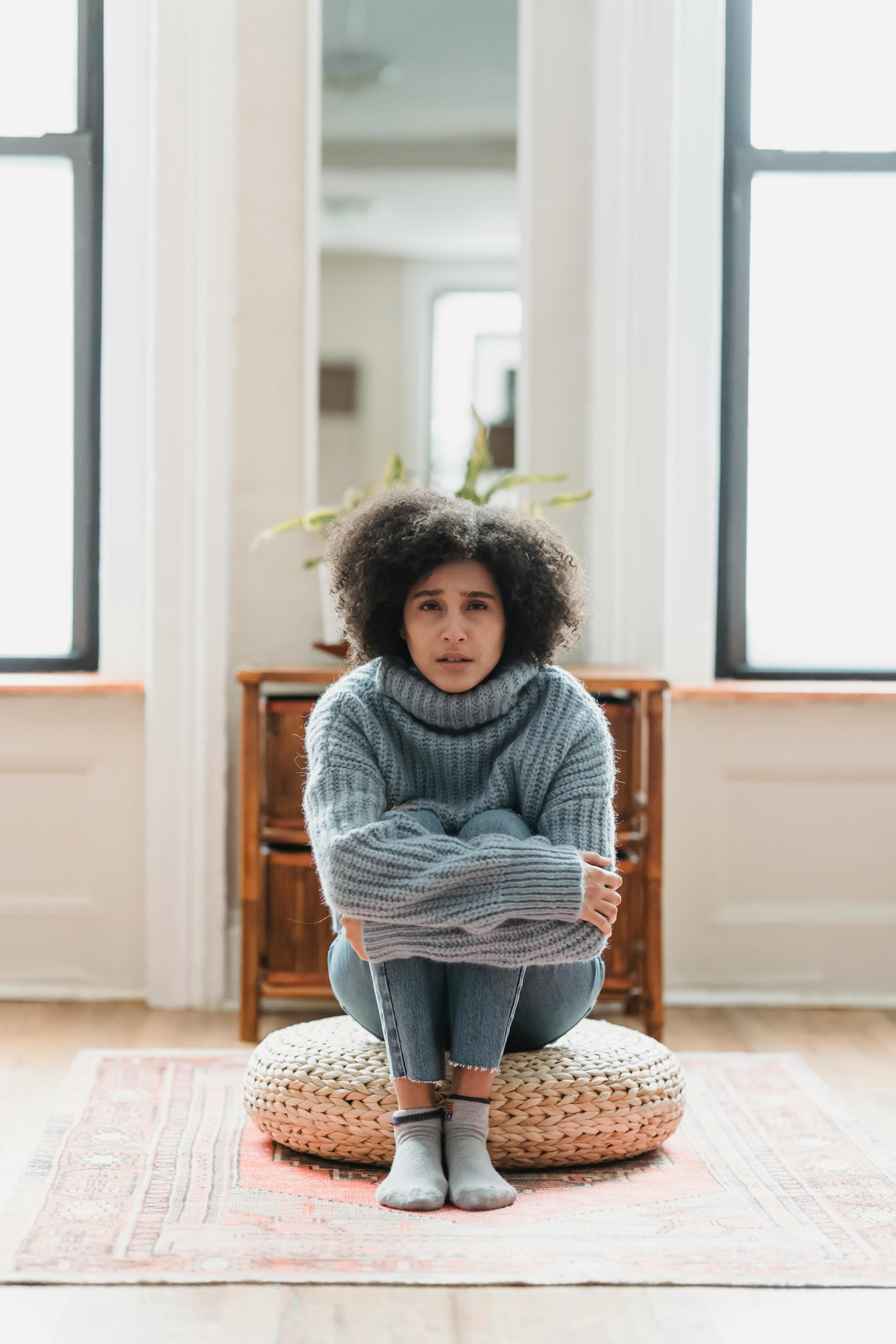 ethnic lady crying on pouf in room near window