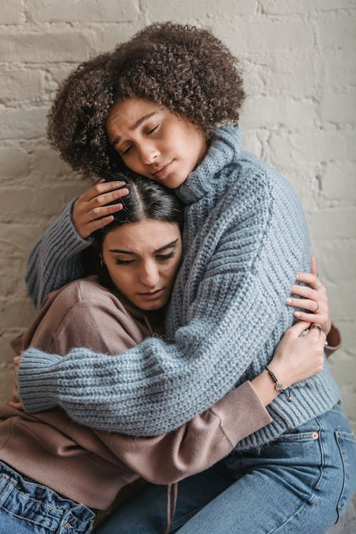 Sad multiethnic women hugging each other while crying at home