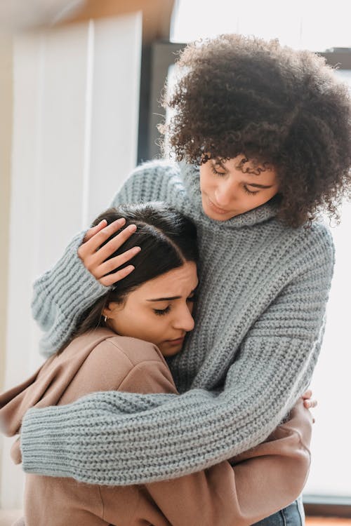 Free Young multiethnic female friends in casual clothes embracing each other while crying in light apartment Stock Photo