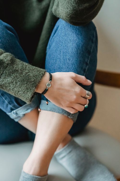 Free Crop anonymous woman in casual clothes and accessories sitting on floor in light apartment with crossed legs Stock Photo