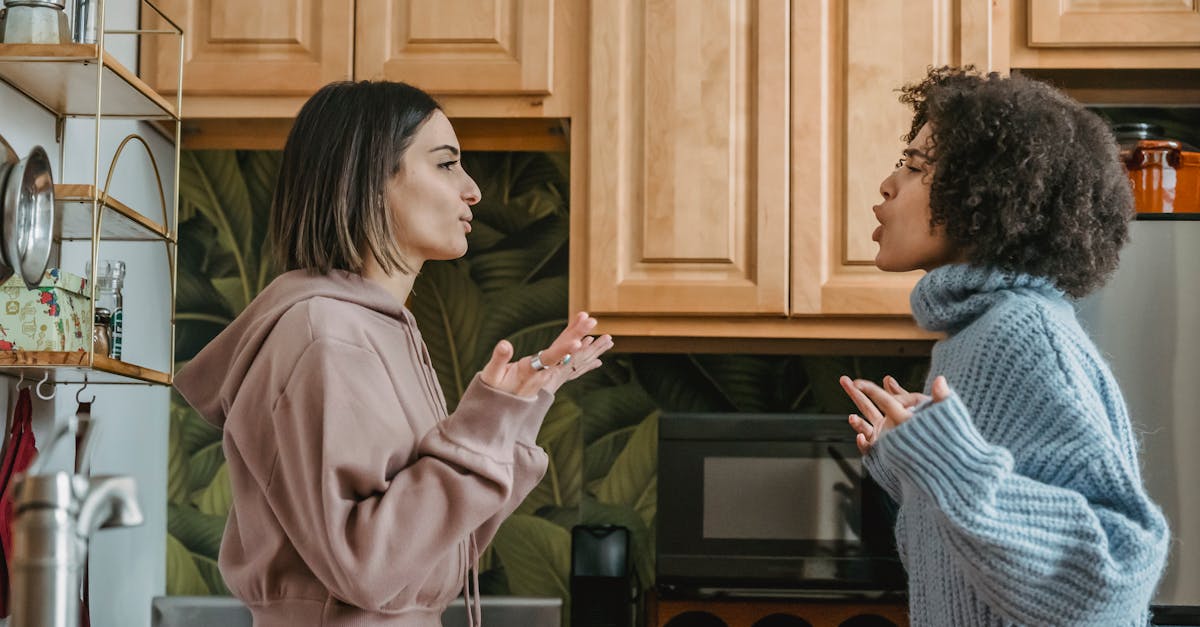 A heated discussion between two young women in a contemporary kitchen setting.
