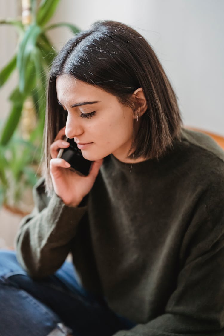 Thoughtful Female In Chair Having Phone Call At Home