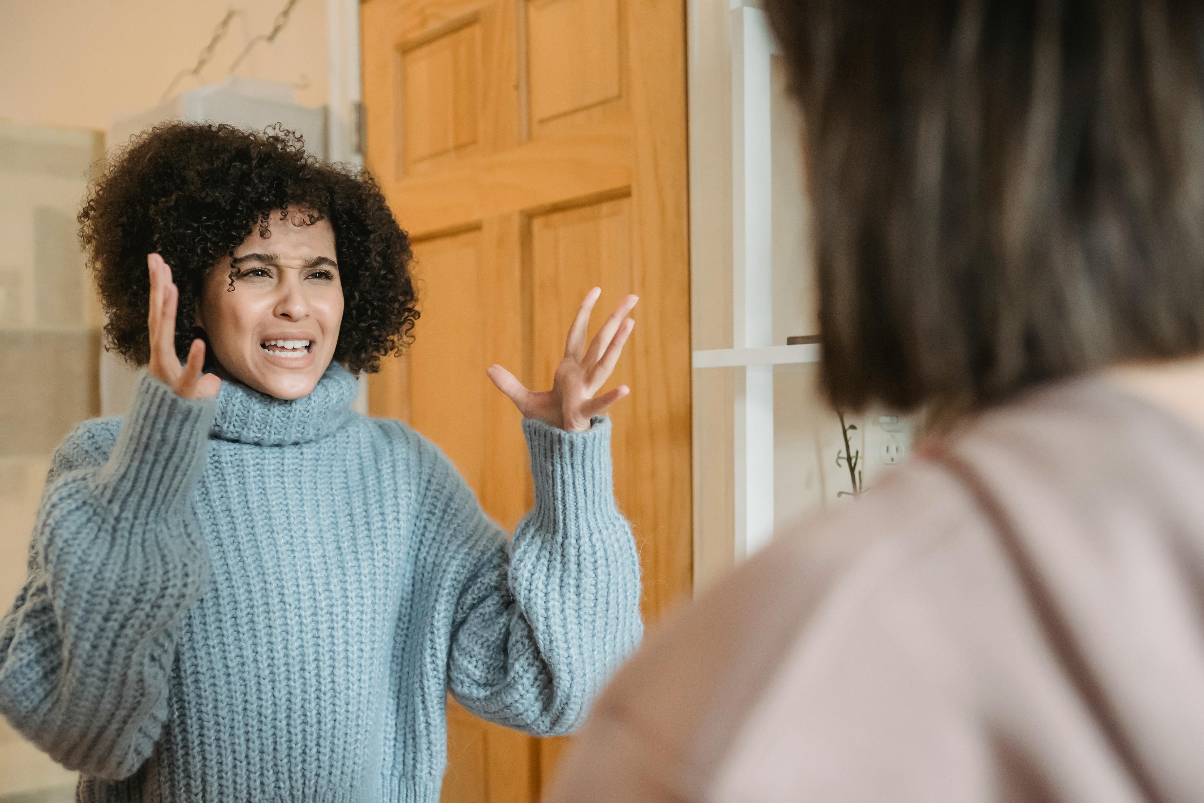 Woman in gray sweater raising both hands defensively with a distressed expression, showing the exhaustion of failed attempts to reason with someone.