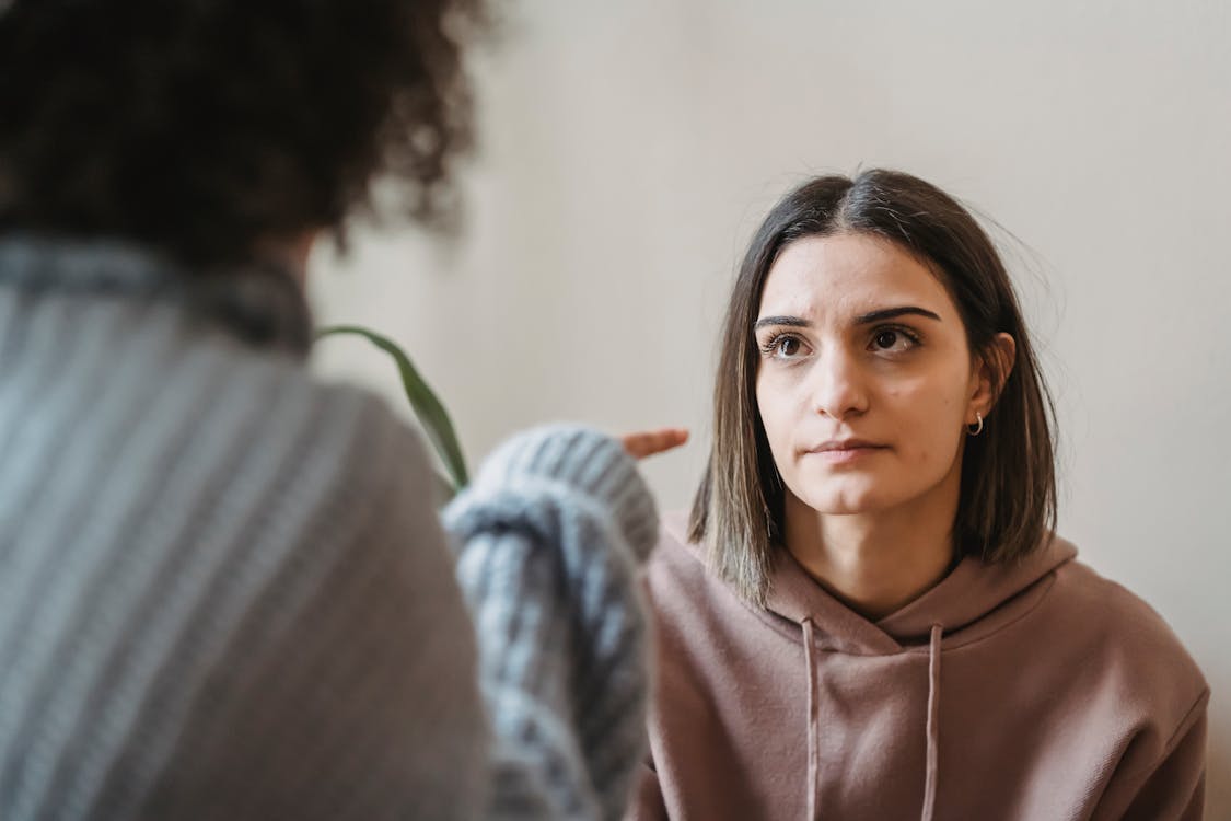 Free Sad young ladies in casual clothes standing in light apartment near wall while having disagreement and pointing finger in face while looking at each other Stock Photo