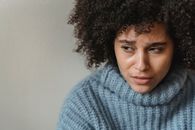 Crying ethnic female with curly hair looking away while thinking over problem and crying near white wall in studio