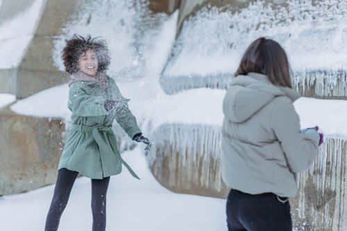 Free Happy ethnic female friends in warm clothes playing snowballs near snowy wall in city Stock Photo