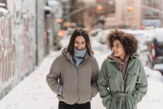 Two friends walking and smiling on a snowy city street. Winter coats and cheerful conversation.