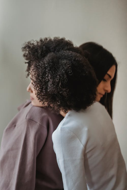 Side view of caring female friends in casual wear embracing while comforting each other near wall in room at home