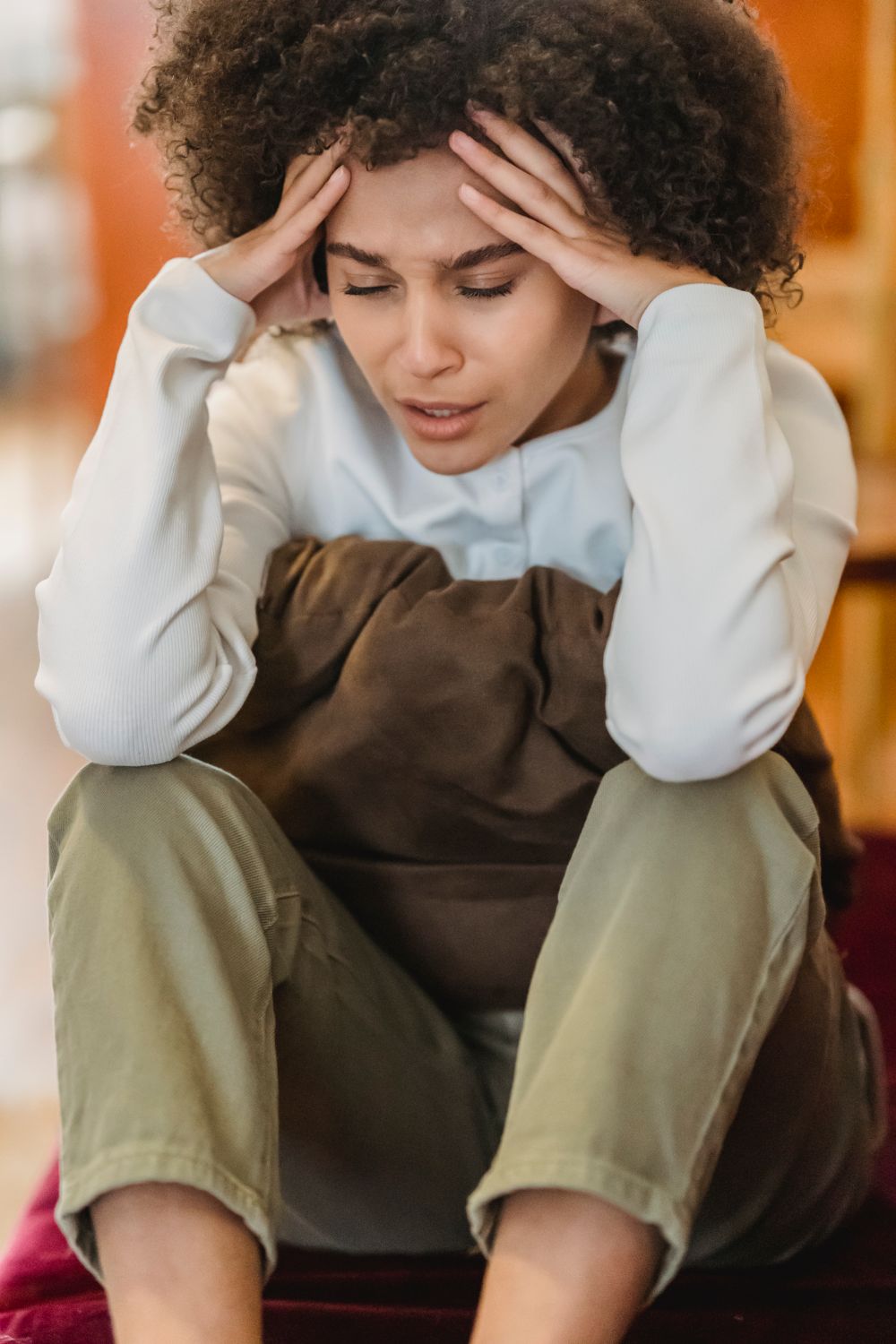 A woman sitting indoors on a couch holding her head with a weary expression