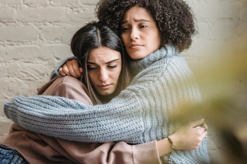 Depressed diverse women hugging near wall