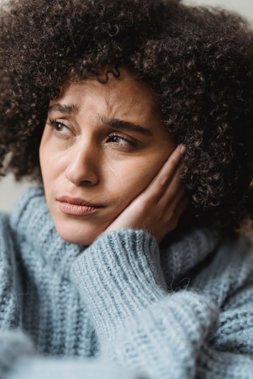 Free Unhappy ethnic female with curly black hair in warm outfit looking away with sorrow while sitting in room at home Stock Photo