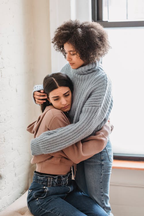 Unhappy diverse women embracing in room